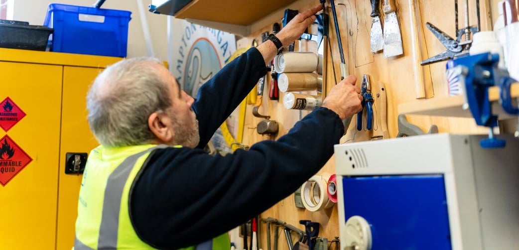 A military veteran turned school caretaker reaches for a saw in a school workshop