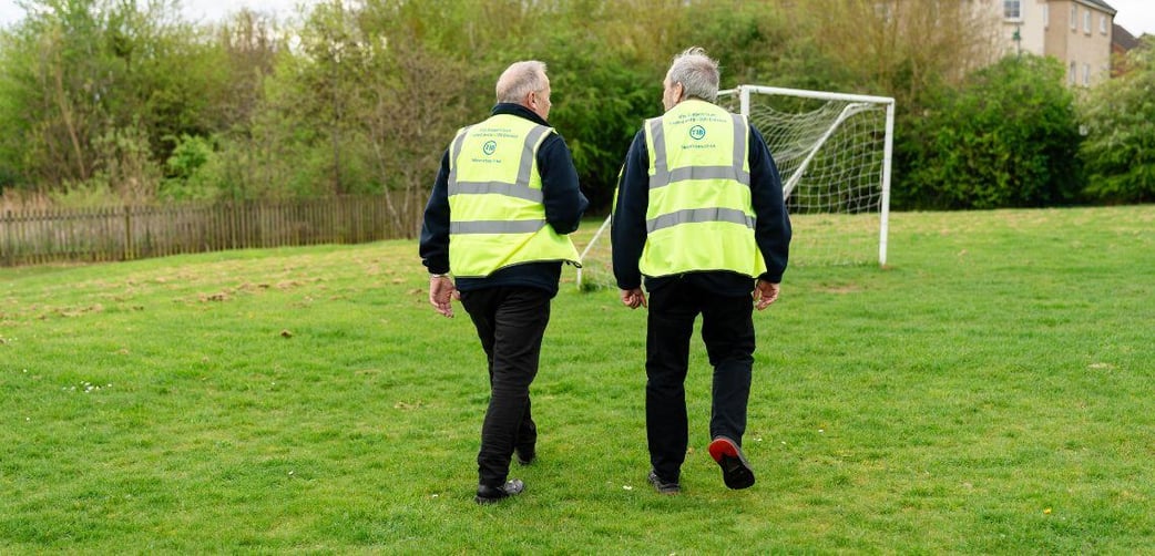 Two TIB Services school caretakers chat while walking across a school playing field