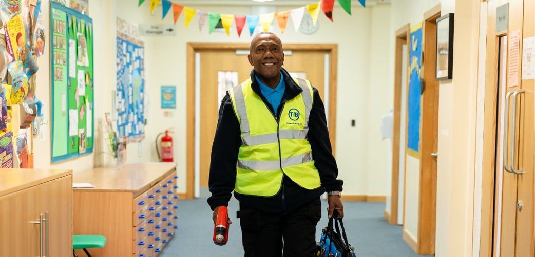 A TIB Services caretaker walks through a tidy school corridor while carrying a toolbox and drill