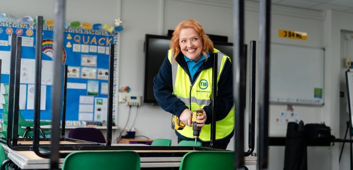 A TIB Services caretaker fixes a school table with a drill