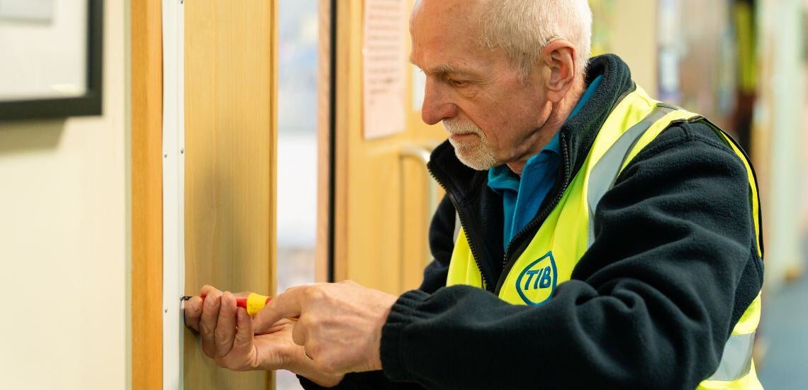 A TIB Services school caretaker fixes tightens a school door with a screwdriver