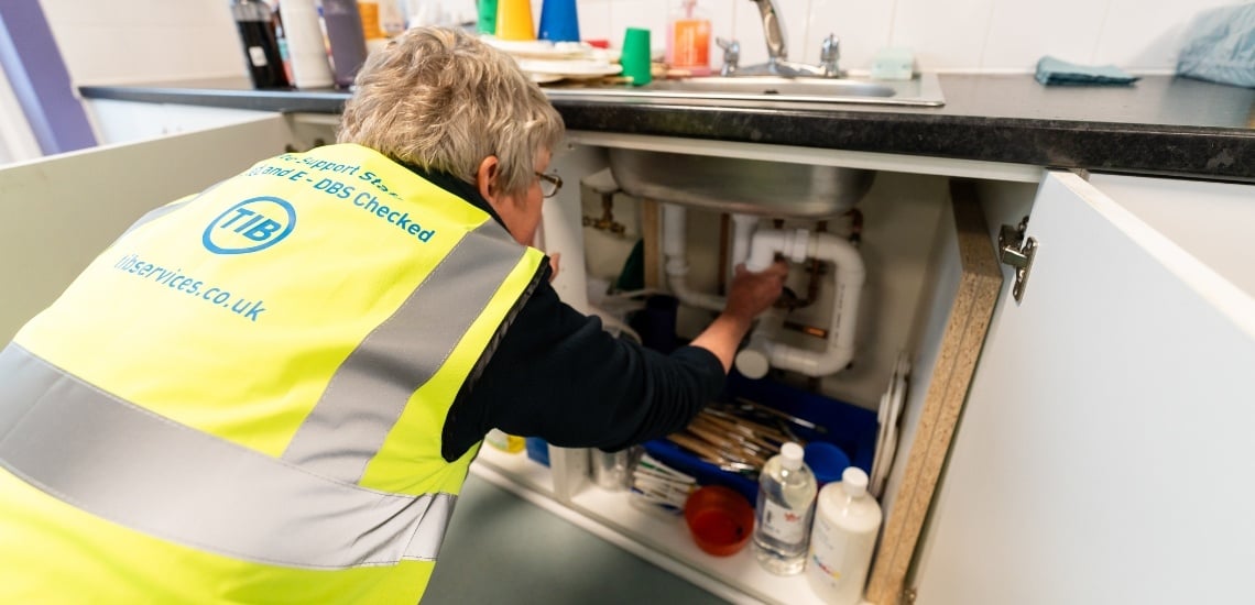 A female TIB Services caretaker fixes a plumbing issue