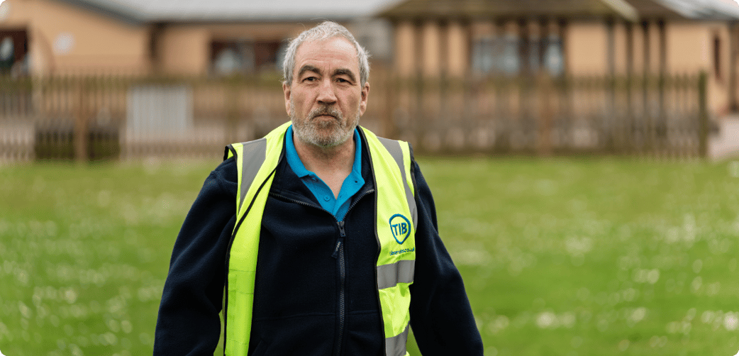 Andy walks across a school playing field while wearing a TIB high vis