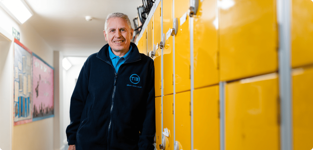 Colin smiles and rests against school lockers while wearing a TIB fleece