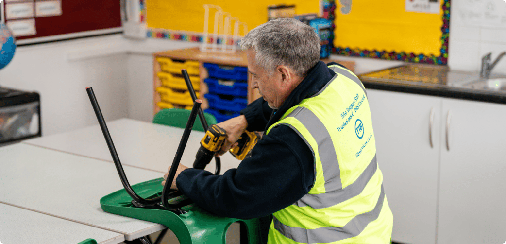 Colin fixes a school chair with a drill while wearing a TIB high vis