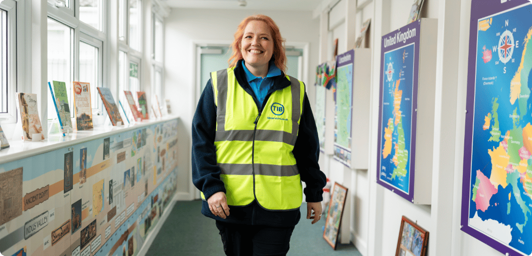 Elizabeth smiles and walks through a school corridor while wearing a TIB high vis