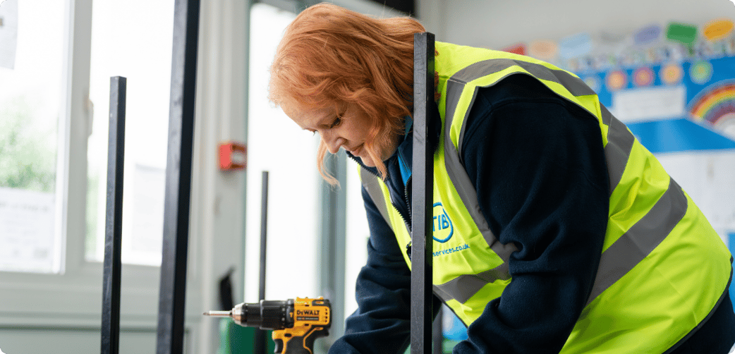 Elizabeth fixes a school table while wearing a TIB high vis