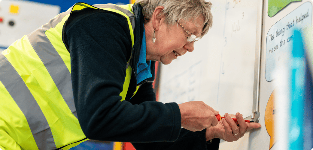 Jan secures a school whiteboard to a wall while wearing a TIB high vis