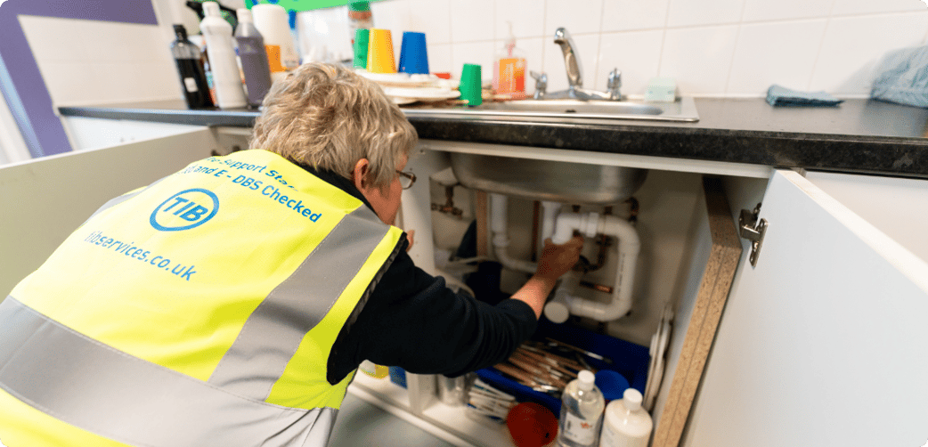 Jan resolves a plumbing issue at a school while wearing a TIB high vis