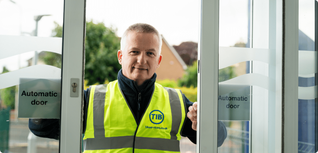 Leigh smiles through a school's automatic doors while wearing a TIB high vis