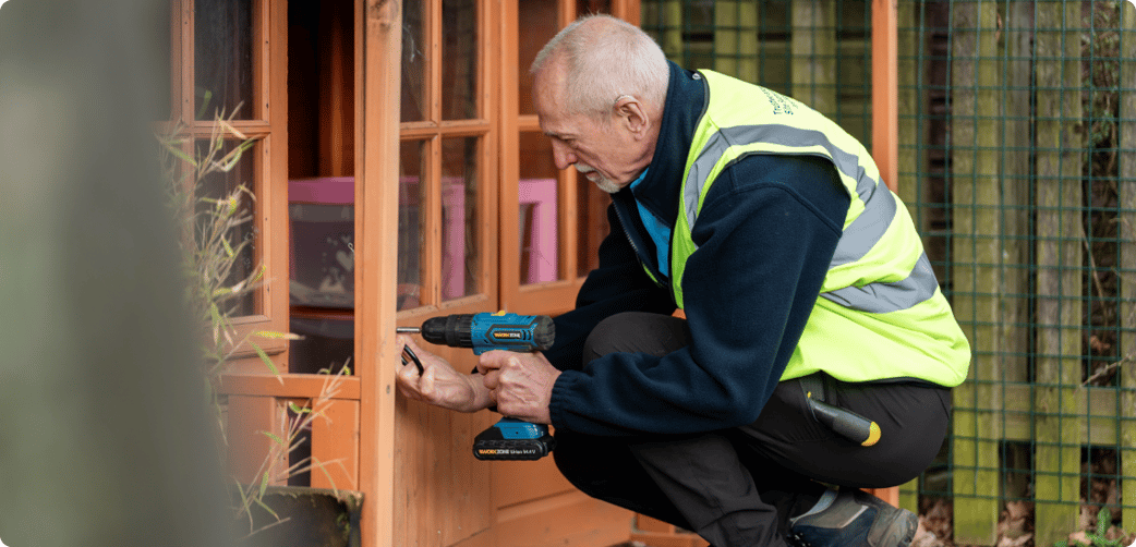 Ted fixes a school's wooden gazebo with a drill while wearing a TIB high vis