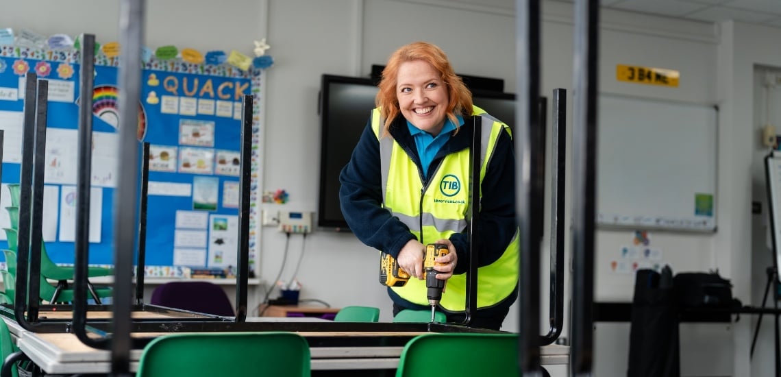 Elizabeth, a female TIB Services caretaker, fixes a school table with a drill