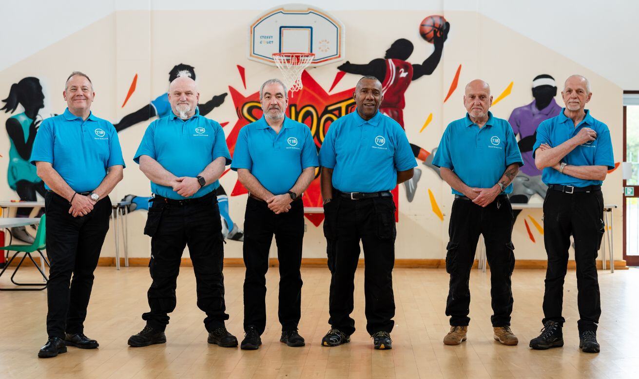 A group of TIB Services school caretakers pose in a line in a school hall