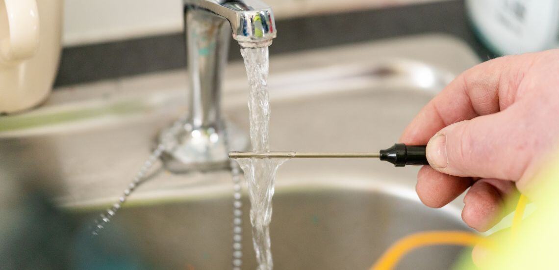 A TIB caretaker tests water at a school