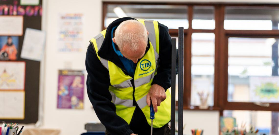 A TIB Services school caretaker fixes a school chair with a screwdriver