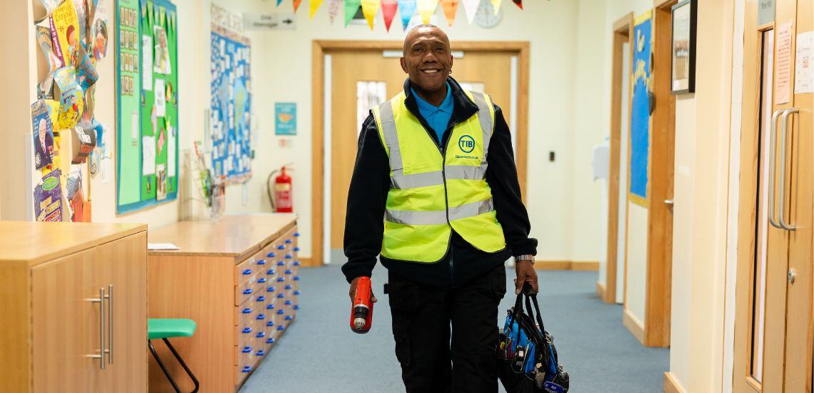 A TIB operative walks through a school corridor in a high vis jacket while holding tools