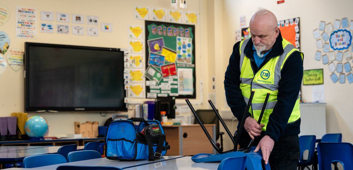 A TIB Services caretaker fixes a school chair in a classroom