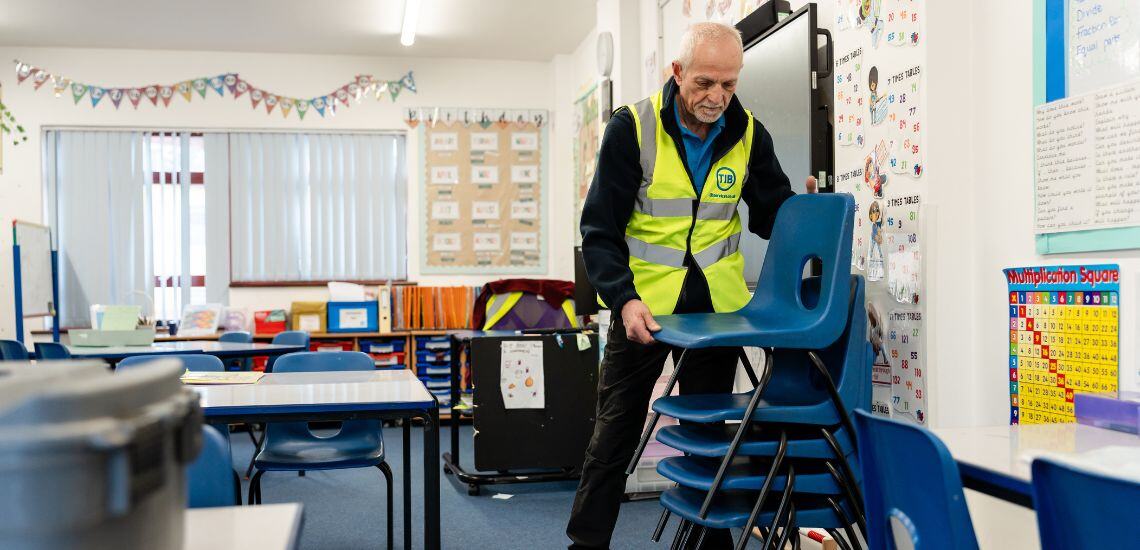 A TIB Services school caretaker stacks school chairs in a classroom