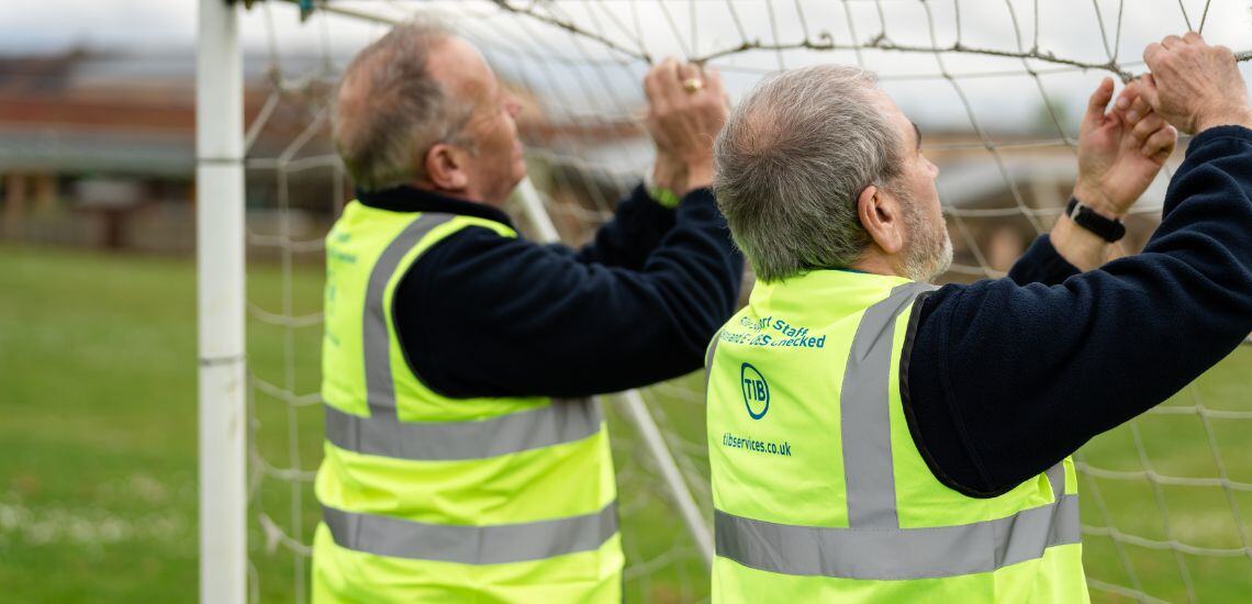 Two TIB Services caretakers fix a football net on a school playfield