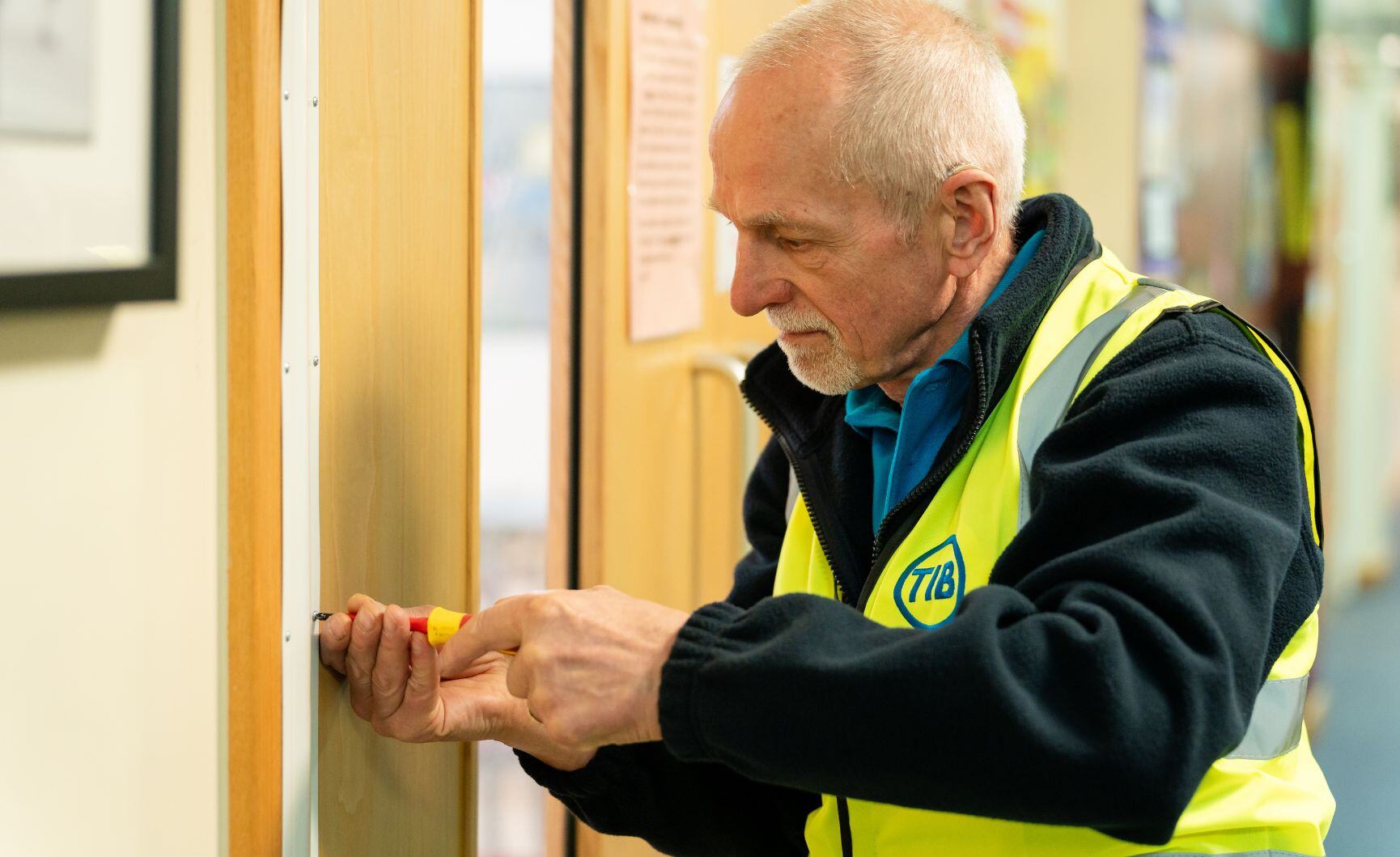 A TIB operative fixes a school door using a screwdriver