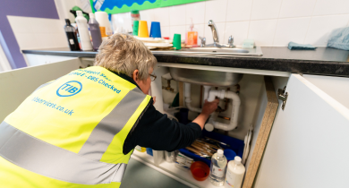 A TIB operative fixes a pipe underneath a sink