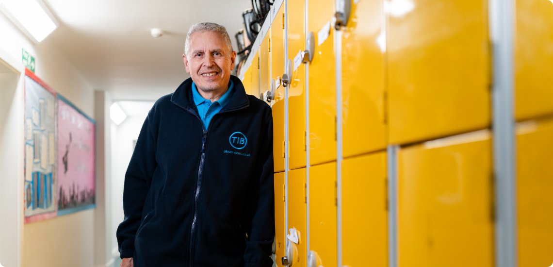 Colin wears a TIB branded fleece while leaning against orange school lockers