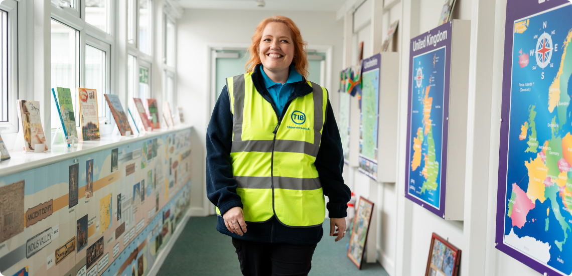 Elizabeth smiles while wearing a TIB high vis and walking through a school corridor