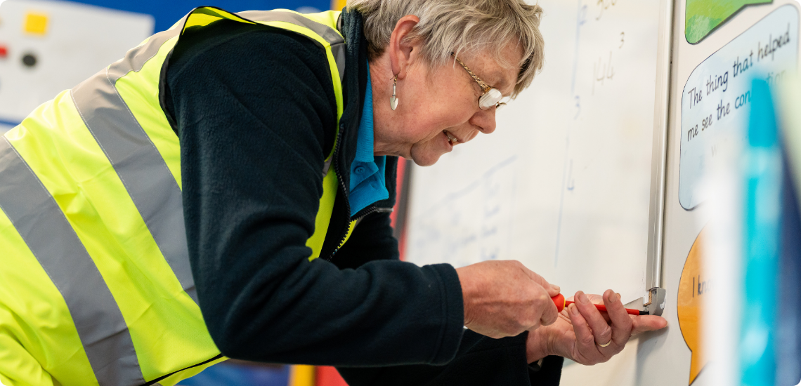 Jan secures a school whiteboard to the wall while wearing a TIB high vis