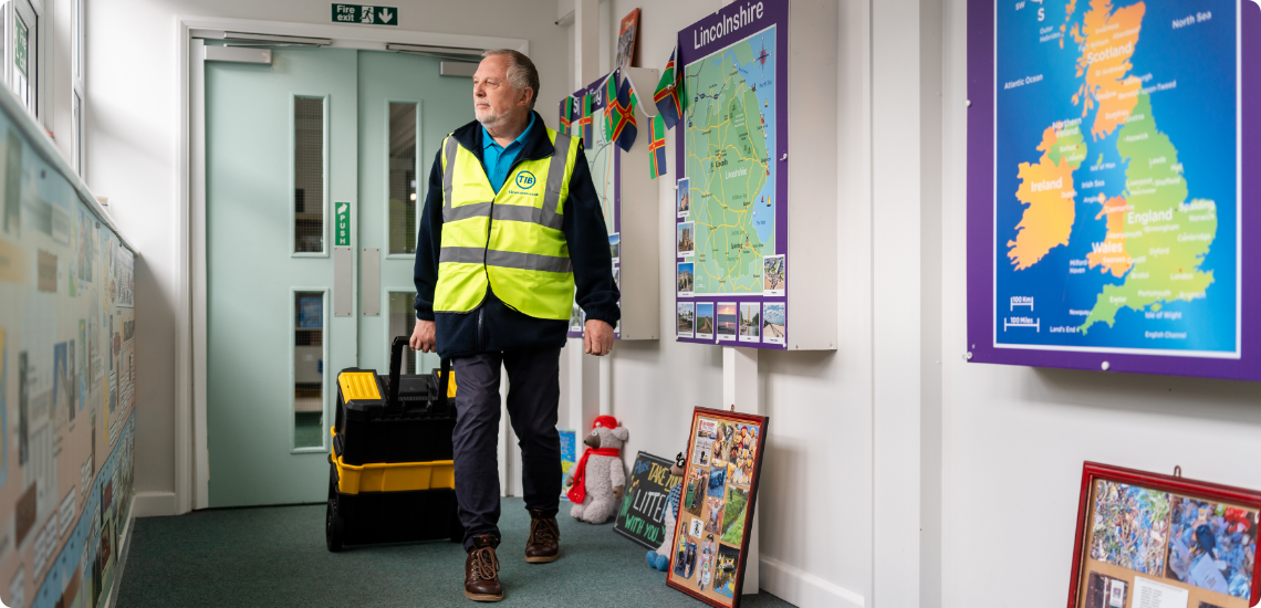 Jeff walks through a school corridor with a toolbox while wearing a TIB high vis